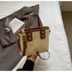 Close-up of cream PU bucket bag with embossed butterfly pattern and brown handles