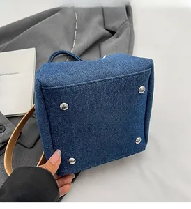 Detail of denim bucket bag bottom featuring four silver metal feet and brown leather strap