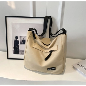 Close-up of beige canvas tote bag featuring black shoulder strap and brand label