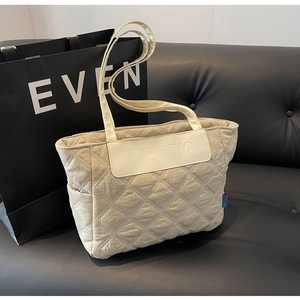 Detailed close-up of quilted beige tote bag featuring a leather SHU NUO brand patch