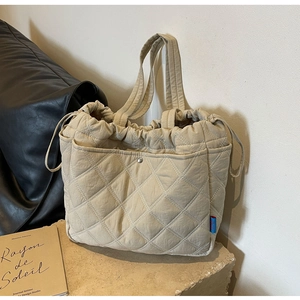 Gros plan du sac cabas matelassé beige avec cordon de serrage sur socle en pierre