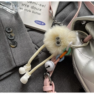 Détail d'un porte-clé monstre en peluche avec clochette sur un sac à dos matelassé argent