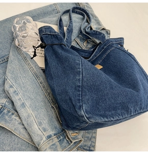 Detail der dunkelblauen Denim-Tragetasche mit Kordelzug und Logo-Tag auf Jeansjacke