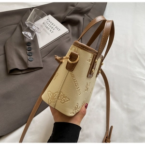 Detail of butterfly embossed beige mini tote bag with brown trim and adjustable strap