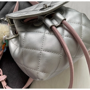 Détail du sac à dos argenté matelassé avec cordon rose, fermoir rotatif et pompon doux