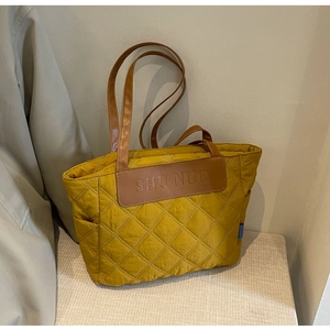Close-up of mustard yellow quilted tote bag featuring brown leather handles and brand patch