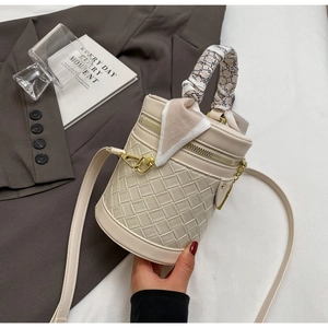 Detail of beige woven leather bucket bag featuring a decorative scarf handle and gold hardware