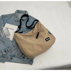 Close-up of khaki nylon tote bag with black strap on denim jacket, minimalist style