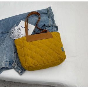 Detail of mustard yellow quilted tote bag with brown leather panel and branded embossing