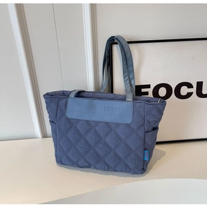 Detail of blue quilted tote bag showing dense stitching and leather logo patch