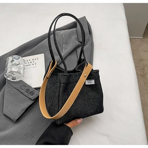 Detail of black denim tote bag with leather strap and logo tag on a grey blazer