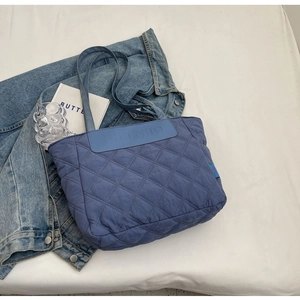 Detailed close-up of blue quilted tote bag with diamond stitching and leather logo patch
