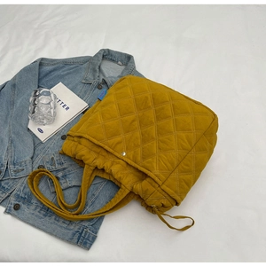 Détail du sac cabas matelassé jaune avec cordons latéraux et bouton pression en métal