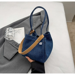 Detail of blue denim bucket bag with brown leather handle in a lifestyle setting