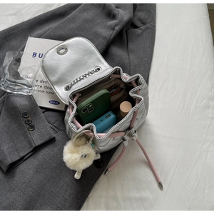 Détail d'un sac seau matelassé argenté avec cordon rose, chaîne et vue sur l'espace intérieur