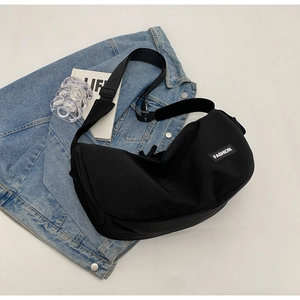 Detail einer schwarzen Nylon-Umhängetasche mit weißem Fashion-Label auf Denim-Stoff