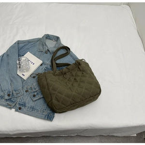 Vue à plat du sac fourre-tout matelassé vert olive avec design plissé sur lit blanc