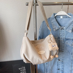 Beige large capacity tote bag with pleated detail and plush monster charm on metal hanger