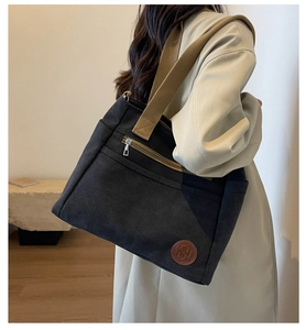 Détail d'un grand sac en toile noir avec fermeture éclair et logo de marque en cuir brun
