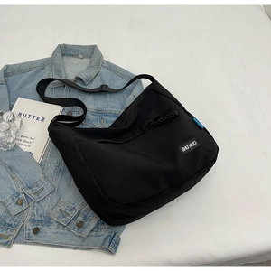 Detail of black nylon tote bag with adjustable strap and logo on light denim jacket