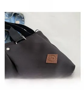 Detail of black canvas tote bag featuring brown leather logo patch and silver D-ring buckle