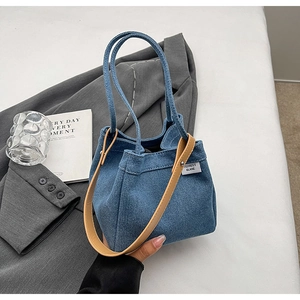 Detail of blue denim tote bag with leather strap and brand label on a gray background
