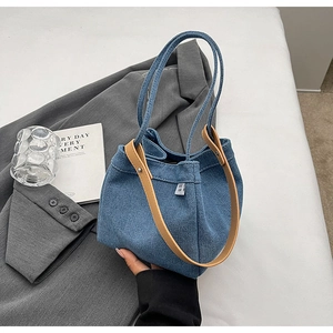 Close-up of denim bucket bag with brown leather handle on grey blazer with a glass
