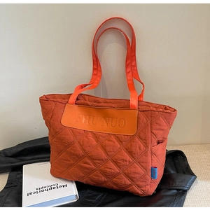 Close-up of quilted tote bag featuring orange leather patch and SHU NUO logo detail