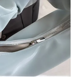 Close-up of a smooth silver metal zipper on a light blue crescent-shaped crossbody bag