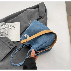 Detail of blue denim bucket bag with leather handle on stylish grey blazer background