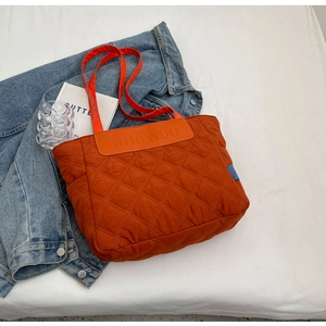 Detailed view of orange quilted tote bag with diamond stitching and shoulder straps