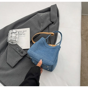 Detail view of denim bucket bag showing brown leather strap and metal bottom studs