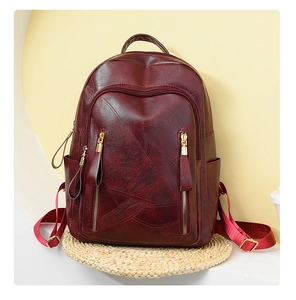 Detail of dark red PU leather backpack with gold zippers on a warm geometric background