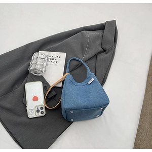 Bottom view of blue denim bucket bag showing four silver protective metal feet and leather strap