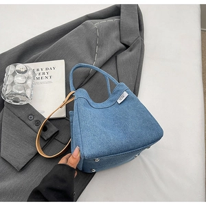 Detailed view of a blue denim bucket bag with leather handle and metal rivets