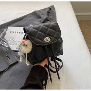 Détail de sac à dos matelassé noir avec fermoir rotatif et pompon fantaisie blanc