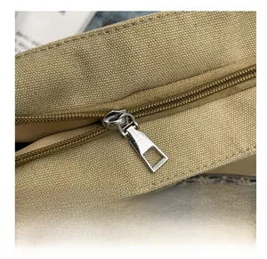 Detailed close-up of smooth silver metal zipper on a khaki canvas tote bag for women
