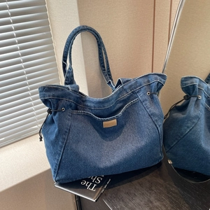 Große dunkelblaue Denim-Tragetasche mit Schultergurten und Lederpatch auf Holzfläche