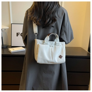 Rear view of a model wearing a white canvas tote bag with adjustable shoulder strap