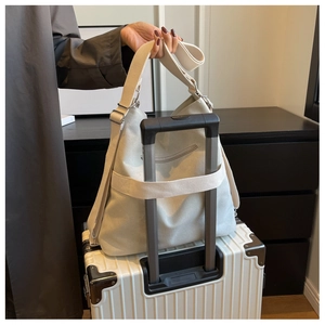 Detailed back view of a canvas travel tote with a luggage strap fixed on a suitcase handle