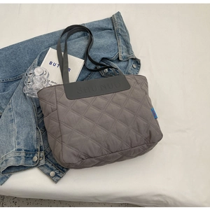 Detail of grey quilted tote bag with diamond stitching on denim jacket backdrop