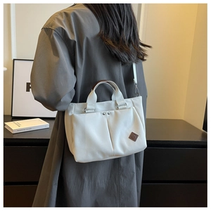 Detail of off-white canvas tote bag with brown handles and dual front pockets worn by model
