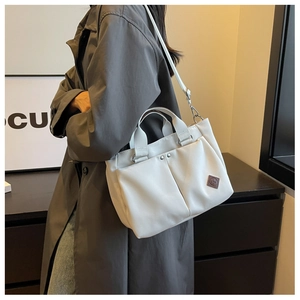 Detail of white nylon tote bag showing dual front pockets and brown leather logo patch