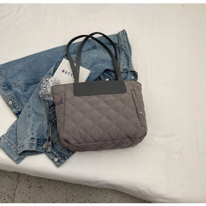 Detailed close-up of grey quilted tote bag with diamond stitching and side zipper