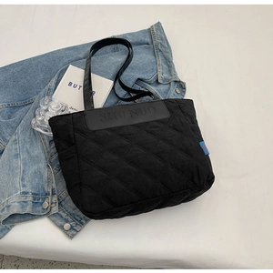 Detail of black quilted tote bag showing diamond stitching and premium leather logo tag