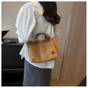 Close-up of khaki canvas tote bag with adjustable leather strap and brown leather badge
