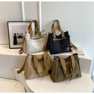 Détail de quatre sacs fourre-tout en toile en beige noir kaki et vert sur socle blanc