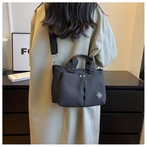 Detail of a black minimalist canvas tote bag featuring pleated front pockets and metal rivets