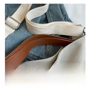 Detail of brown leather handles and adjustable fabric strap on canvas tote bag