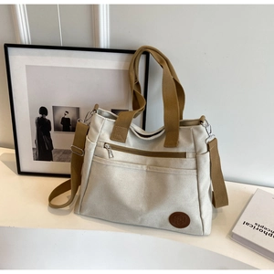 Détail du sac fourre-tout en toile avec anses brunes, poche zippée et bandoulière réglable